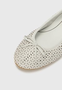 Vit perforerad läderballettsko med rund tå, båge i framkant och en lätt sula. Har ett intrikat utskärmningsmönster för andningsförmåga.