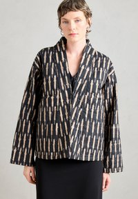 Jachetă neagră matlasată cu un model abstract bej, având mâneci largi, decolteu în v și buzunare frontale, confecționată dintr-un material texturat.