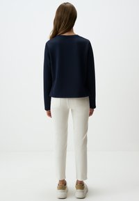 Felpa blu navy con maniche lunghe, colletto rotondo, abbinata a jeans attillati color crema e sneakers bianche con accenti nocciola.