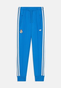Blauwe sportbroeken gemaakt van een gladde stof, met witte zijstreepjes, ritszakken en logo's: Real Madrid en Adidas aan de voorkant.
