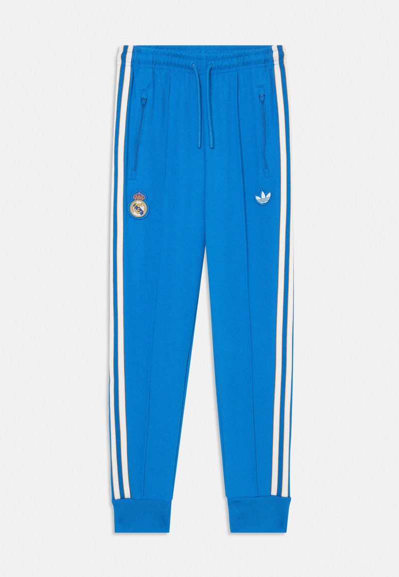Blauwe sportbroeken gemaakt van een gladde stof, met witte zijstreepjes, ritszakken en logo's: Real Madrid en Adidas aan de voorkant.