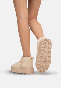 Botas de tobillo beige hechas de suave ante presentan una gruesa suela de plataforma con textura antideslizante. Se pueden ver las costuras y una pestaña en la parte trasera.