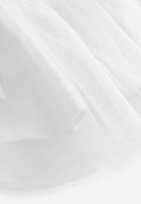 Detailní záběr průsvitné bílé látky s jemnými, plynulými záhyby a křehkou, průhlednou texturou.