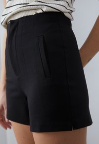 Čierne elegantné šortky s bočnými vreckami, hladkou textúrou a čistým vzhľadom, s jemným rozparkom na leme pre komfortnejší pohyb.