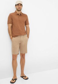 Brun polo shirt, beige shorts, sorte flip-flops. Enkel design, korte ærmer og krave. Let stof med glat tekstur.