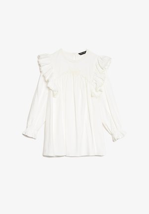 Blouse blanche à manches longues avec des accents à volants et un col rond. Comprend des détails texturés et un tissu froncé au niveau de la poitrine.