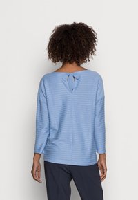 Jasnoniebieski sweter w paski z szerokim dekoltem, rękawami o długości trzech czwartek oraz zawiązywaniem na plecach. Miękka faktura i luźny krój.