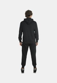 Felpa nera con cappuccio abbinata a pantaloni jogger coordinati, dotati di tasche laterali e polsini a coste, mostrata da dietro.