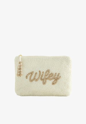 Krémově zbarvená kabelka s korálky se zlatým nápisem "Wifey" a odpovídajícím zlatým a krémovým střapcem na zipu.