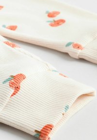 Geripptes Baumwollgewebe in Creme mit orangefarbenen Obstmustern und grünen Blättern. Umschlagmanschetten zeigen Details der strukturierten Oberfläche.