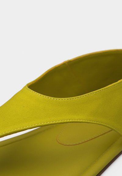 Κοντινό πλάνο ενός σανδαλιού από σουέτ σε λάιμ πράσινο χρώμα, με φαρδιά λουριά στο επάνω μέρος και λεία εσωτερική σόλα.