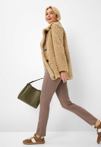 Fuzzy beige frakke med store sorte knapper, parret med brune tætsiddende bukser og brune sneakers med hvide detaljer. Olivengrøn håndtaske.