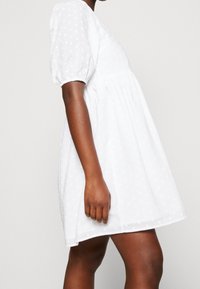 Vestido blanco de mangas abullonadas con textura de puntos, falda acampanada y corsé ajustado. Tejido suave, hasta la rodilla y escote redondeado.