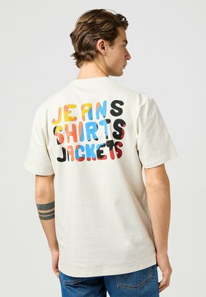 Witte katoenen T-shirt met op de achterkant meerkleurige blokletters: "JEANS SHIRTS JACKETS." Regelmatige pasvorm met korte mouwen en een ronde hals.