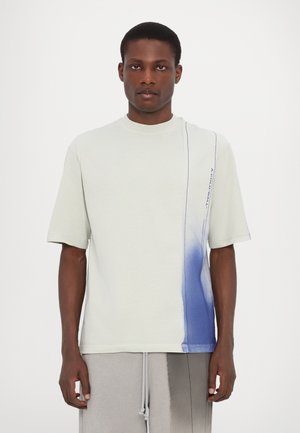Camiseta de algodón gris claro con un diseño de degradado azul en el lado izquierdo y un logo sutil, con mangas cortas y escote redondo.