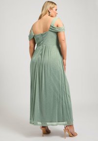 Mintinvihreä, hohtava maksimekko, jossa on olkaimettomat hihat, pleatattu selkä ja istuva yläosa, yhdistettynä nudenvärisiin korkokenkiin.