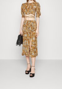 Leopardmuster-Crop-Top und Midirock-Set in Gelb, Braun und Weiß; Puffärmel; Schlitze an der Seite; kombiniert mit schwarzen Plateau-Heels und einer Handtasche.