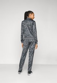 Grå leopardmönstrad träningsoverall i slät tyg, med en zip-jacka och avsmalnande byxor med sidostripes, kombinerad med svarta sneakers.