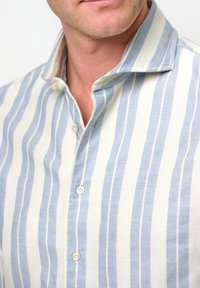 Camicia azzurra chiara a righe bianche con colletto a punta. Texture morbida, vestibilità casual e tre bottoni visibili sul pattino.