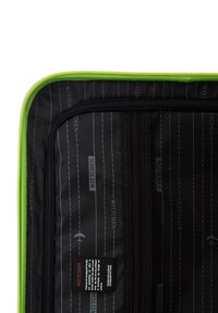 Zwart interieur van een koffer met groene rits. Bevat merpattern, een gaasvak en een onderhoudsetiket met productinformatie.