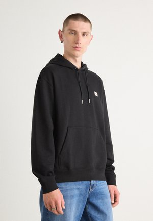 Zwarte pullover hoodie met een voorkant kangaroo-zak en trekkoorden. Beschikt over een klein logo-badge en geribbelde manchetten, gecombineerd met blauwe spijkerbroek.