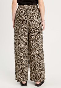 Pantalons à larges jambes en imprimé léopard beige et noir, avec une taille élastique et un tissu lisse. Portés avec des chaussures foncées.