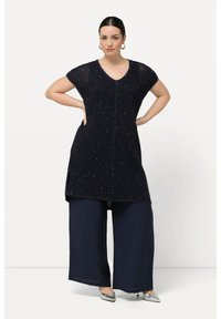 Túnica navy de manga corta y cuello en V, con un patrón texturizado y embellishments, combinada con pantalones de pierna ancha en navy y zapatos plateados.