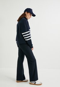Navy oversized sweatshirt met witte strepen op de mouwen, gecombineerd met wijdvallende navy broek en witte sneakers met zwarte accenten.