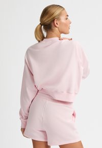 Felpa rosa con design cropped, maniche e orlo a costine, abbinata a pantaloni corti rosa coordinati. Tessuto morbido, stile semplice e minimalista.