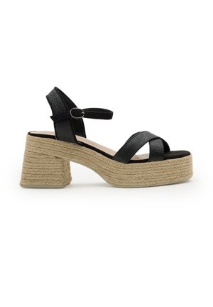 Sandalia negra de tiras trenzadas con hebilla en el tobillo, plataforma y tacón ancho envueltos en material de yute trenzado.