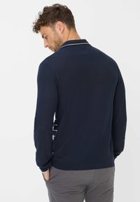 Navyblaues Langarm-Polohemd mit gestreiftem Kragen, das einen strukturierten Stoff zeigt. Die Rückseite weist ein einfaches Design und eine taillierte Silhouette auf.