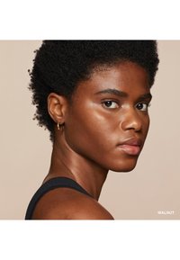 Vue de profil d'une personne avec des cheveux sombres et texturés, ayant une peau brun moyen, portant un haut noir et des boucles d'oreilles en or, avec une peau lisse et des traits bien définis.