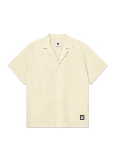 Chemise à manches courtes de couleur beige clair, fabriquée dans un tissu doux. Elle possède un col évasé, des boutons sur le devant et deux poches avant. Logo dans le coin inférieur.