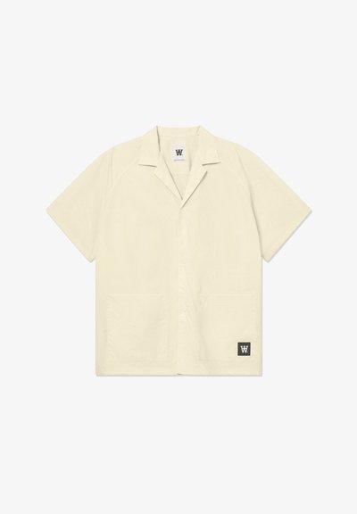 Chemise à manches courtes de couleur beige clair, fabriquée dans un tissu doux. Elle possède un col évasé, des boutons sur le devant et deux poches avant. Logo dans le coin inférieur.
