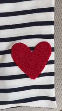Tissu rayé présentant des lignes horizontales bleues marine et blanches, avec une application en forme de cœur texturé et en peluche de couleur rouge sur le côté gauche.
