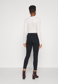 Jeans ajustados de mezclilla oscura con bolsillos traseros, cintura alta, combinados con botas de tobillo burdeos. Textura suave y diseño ajustado.