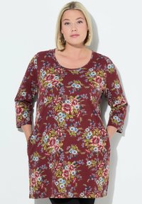 Bordeauxfarbene Blusentunika mit drei Viertelärmeln, die blaue und rosa Blumen zeigt, runder Ausschnitt und Seitentaschen hat. Aus weichem, leichtem Stoff.