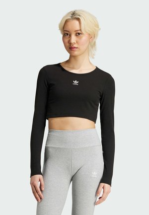 Svart kortärmad långärmad tröja med ribbad textur och vit Adidas-logga på bröstet. Matcher med grå högmidjade leggings.