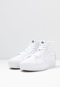 Vita höga sneakers i slätt läder med snörning, vadderad krage och signaturdetalj med rand på sidan. Platt gummisula.