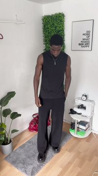 Black sleeveless top paired with loose black pants. Smooth texture, minimal design. Worn with black shoes, standing on a gray rug.