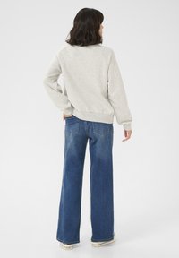 Grauer Pullover mit rundem Halsausschnitt und langen Ärmeln, kombiniert mit blauen weit geschnittenen Jeans. Das Outfit ist lässig und hat eine entspannte Passform.