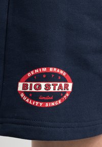 Námořnická modrá tkanina má kruhové červené a bílé logo s nápisem "BIG STAR" a datem založení 1979. Měkký, texturovaný povrch.