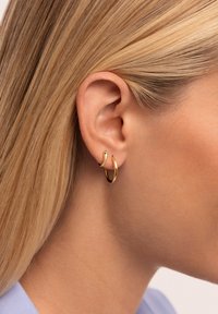 Aros de oro en forma de aro exhibidos en la oreja de un modelo; un aro presenta un diseño texturizado, proporcionando contraste visual con el aro liso.