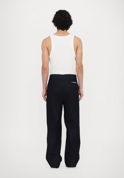 Dark blue denim trousers with a relaxed fit, featuring a waistband with belt loops and a back pocket with 'LES' embroidery.