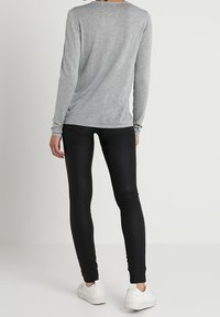 Šedé tričko s dlouhým rukávem a kulatým výstřihem, doplněné těsnými černými legínami a bílými teniskami, pohled zezadu.