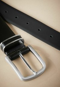 Cinturón de cuero negro con hebilla de metal plateado, que cuenta con múltiples agujeros de ajuste y una textura suave. Detalles de costura cerca de la hebilla.