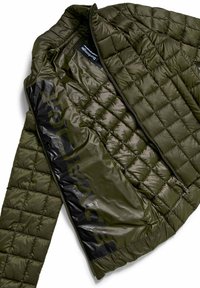 Oliwkowa pikowana kurtka z błyszczącą podszewką, z pełnym zamkiem błyskawicznym, teksturowanym zewnętrzem i wyraźnym logo od wewnątrz.