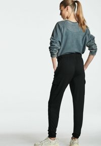 Sudadera gris oscuro con mangas extragrandes y puños acanalados, combinada con joggers negros con bolsillos tipo cargo. Zapatillas completan el look.