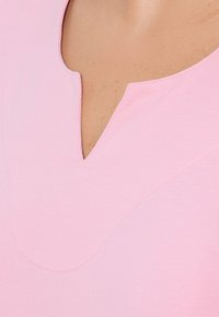 Top rosa a V in tessuto morbido con dettagli di cucitura sottili. Texture liscia con leggero luccichio, senza motivi o accessori visibili.