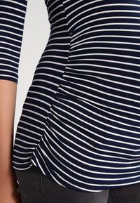 Navyblau gestreiftes Oberteil mit weißen horizontalen Linien, das über ein figurbetontes Design, 3/4-Ärmel und seitliche Raffung für einen gerafften Effekt verfügt.